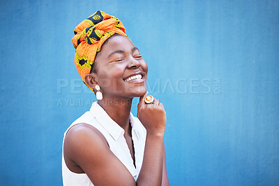 Buy stock photo Fashion, style and trendy african woman on a blue wall or background with a headwrap. African american headwear, trend and beauty with a female fashion stylist in contemporary apparel and jewelry 