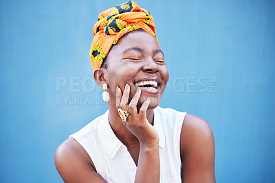 Buy stock photo Happy black woman, african fashion and culture with turban scarf on blue wall background in Nigeria. Happiness, beauty and cultural style of young black person laughing with jewelry, makeup and smile