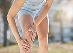 Woman, leg and knee injury or pain from running exercise, workout or sports accident during training in the outdoors. Female hands holding painful, sore or bruise area from run or cardio exercising