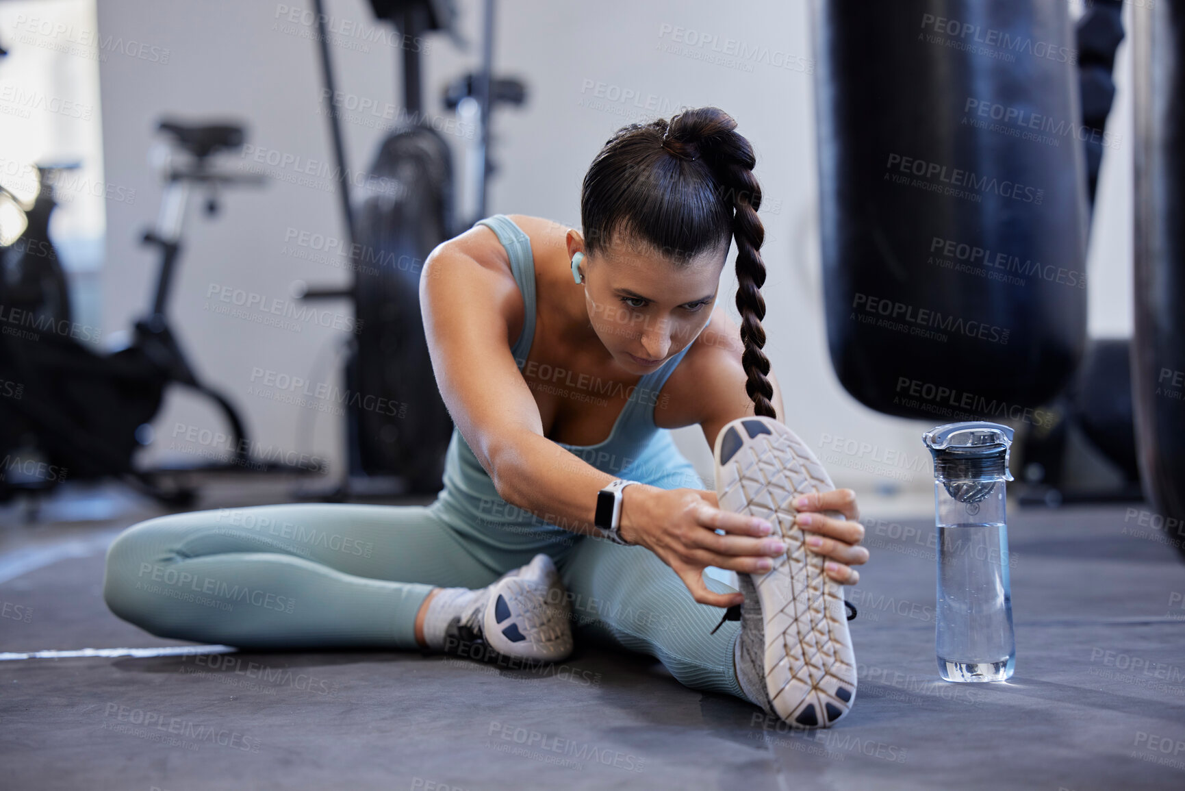 Buy stock photo Fitness, stretching and legs of woman in gym with water bottle and audio for muscle training, energy and workout challenge in focus. Warm up exercise, body goals and sports athlete listening to music