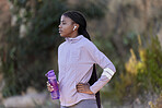 Fitness, running and black woman with water bottle in nature for wellness, minerals and healthy lifestyle. Exercise, sports and girl with earphones rest, breathe and relax after marathon training 