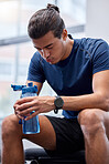 Fitness, tired or man at gym drinking water, breathing or relaxing on a exercise, workout or cardio training break. Fatigue, wellness or healthy sports athlete resting on bench with bottle of liquid 