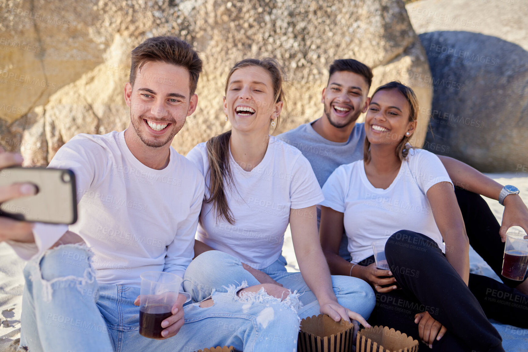 Buy stock photo Couple of friends, selfie and drinks on a beach picnic with a smile for a social media update while on vacation in summer. Men and women with phone on double date at rocks for fun and freedom outdoor