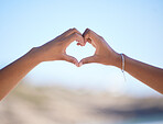 Hands together, heart sign and outdoor at beach, nature and blue sky in blurred background for love. Couple, hand touch and romantic gesture for bonding, care and support for relationship in Miami