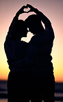 Love, heart hands and couple silhouette at beach during sunset, summer care and happy on holiday in Bali. Emoji, dark and man and woman with happiness, affection and sign on honeymoon at the ocean