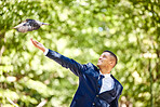 Business man, bird and nature park for freedom, success and start of new opportunity as leader while outdoor with a smile and happiness. Entrepreneur with animal on green tree background for hope