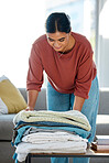 Woman, fold laundry and table in home with clean towel, fabric or tidy for hospitality with smile. Happy cleaner, cotton and textile in lounge for cleaning clothes for hygiene, job and housekeeping