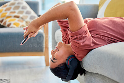 Buy stock photo Woman, phone and sofa with smile, upside down and reading on web, app or social media in lounge. Happy gen z girl, headphones and smartphone for music, streaming or relax on couch in home living room
