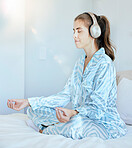 Yoga, meditation or zen woman in bedroom with headphones streaming relaxing radio, calm music or podcast. Peace, mental health or spiritual girl in lotus pose to meditate for mindfulness or wellness