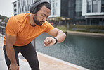 Fitness, headphones and watch with black man checking running, training and exercise time. Urban, runner and sports athlete listening to music, audio or podcast by water looking at heart rate health