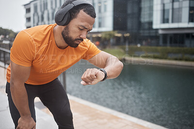 Buy stock photo Fitness, headphones and watch with black man checking running, training and exercise time. Urban, runner and sports athlete listening to music, audio or podcast by water looking at heart rate health