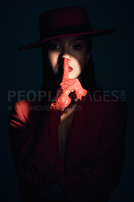 Buy stock photo Fashion, silence and woman in red suit on a dark studio background. Quiet, spotlight and face portrait of beautiful, vintage or 90s female model in makeup cosmetics with shush hand gesture for peace.