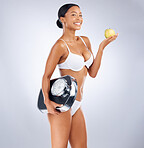 Health, diet and woman with a scale and apple for nutrition wellness snack posing in a studio. Portrait of a girl model from Mexico with a organic, raw and healthy fruit isolated by a gray background