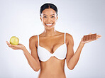 Black woman, portrait smile and body in diet plan for healthy skincare or vitamins against a grey studio background. Happy woman smiling in bra holding apple and chocolate in weight loss or bodycare