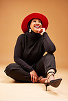 Fashion, beauty and muslim woman in hat in studio on a brown background. Vintage aesthetic, mature or Islamic female model laughing, sitting on floor and thinking of classy, stylish or retro clothing