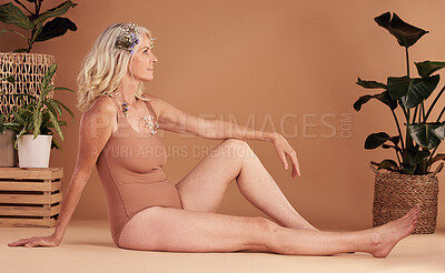 Buy stock photo Beauty, real and natural with a senior woman in studio on a brown background with plants for body care. Wellness, luxury and thinking with an attractive mature female sitting on the floor for health