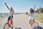 Couple, bicycle and celebrate happiness for freedom on beach, travel holiday and summer vacation. Happy man, woman smile and cycling bike, cheerful and laughing together for love in ocean sidewalk