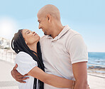 Love, hug and happy couple at beach promenade for summer vacation, holiday and freedom in sunshine. Man, woman and people hugging outdoor at ocean sidewalk for travel, peace and happiness together 