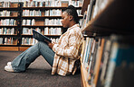 Library, college student and black woman reading books on ground floor for education, studying and campus learning. University student, girl and bookshelf for project, knowledge and academy research