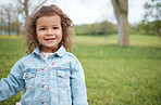 Child, face and park with grass field while outdoor for fun, travel and freedom in spring on vacation with smile, happiness and positive energy. Face of cute girl in nature with green background