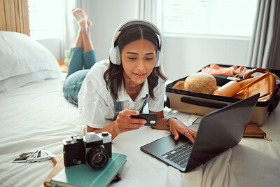 Buy stock photo Travel, woman and bedroom booking on laptop with credit card for holiday planning with music streaming. Vacation preparation and online payment of girl with headphones on bed with luggage in home.

