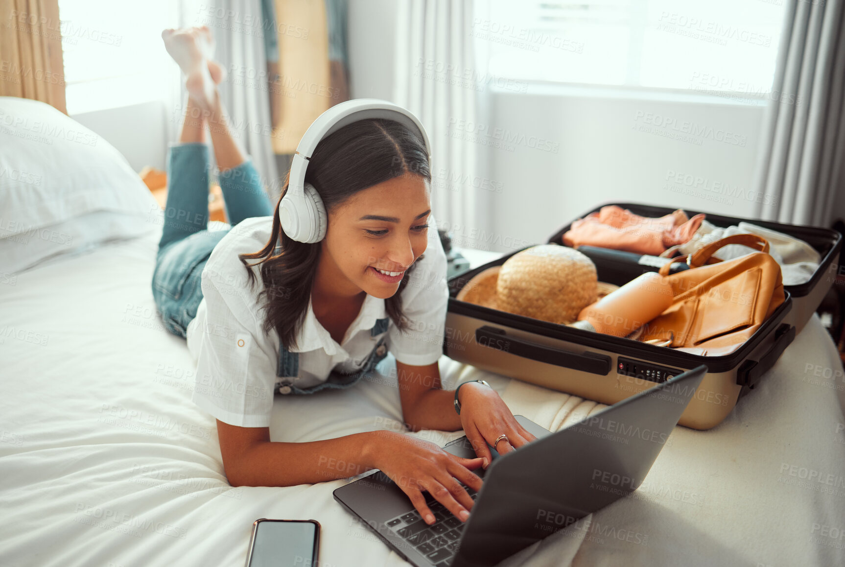 Buy stock photo Computer travel and woman packing for a vacation with headphones typing a holiday blog. Adventure, planning and female happy on a hotel room bed with a luggage, suitcase and bag ready for a journey