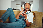 Young girl, headphones and music with smartphone, relax at home with technology and listening to podcast, radio and audio streaming. Online, social network and happy on sofa with sound and wellness.