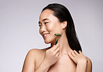 Jade roller, skincare and woman with face massage, dermatology beauty and luxury wellness on a studio background. Spa health, happy and Asian model marketing a massaging product for skin health