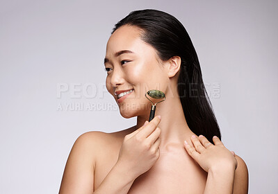 Buy stock photo Jade roller, skincare and woman with face massage, dermatology beauty and luxury wellness on a studio background. Spa health, happy and Asian model marketing a massaging product for skin health