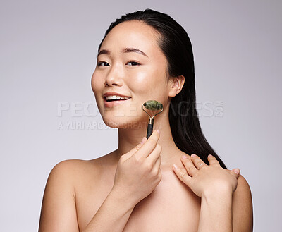 Buy stock photo Jade roller, face massage and woman with skincare marketing, dermatology beauty and spa glow on a grey studio background. Facial, cosmetics and portrait of an Asian model with a massaging product