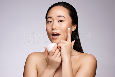 Buy stock photo Face, skincare and product with a model asian woman in studio on a gray background to apply lotion to her skin. Portrait, beauty and cosmetics with an attractive young female applying moisturizer