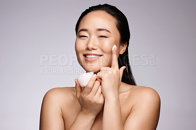Buy stock photo Skincare, cream and woman with beauty smile, spa cosmetics and wellness on a grey studio background. Cosmetic, luxury and face portrait of an Asian model advertising a lotion or sunscreen product
