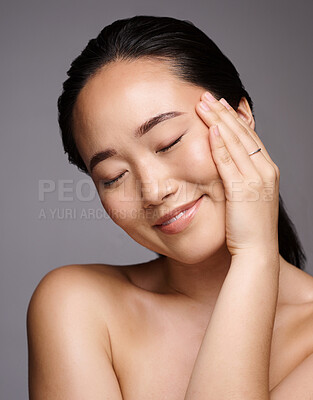 Buy stock photo Face, beauty and skincare with a model asian woman touching her skin in studio on a gray background. Relax, wellness or cosmetics with an attractive young female posing for a luxury skin care product
