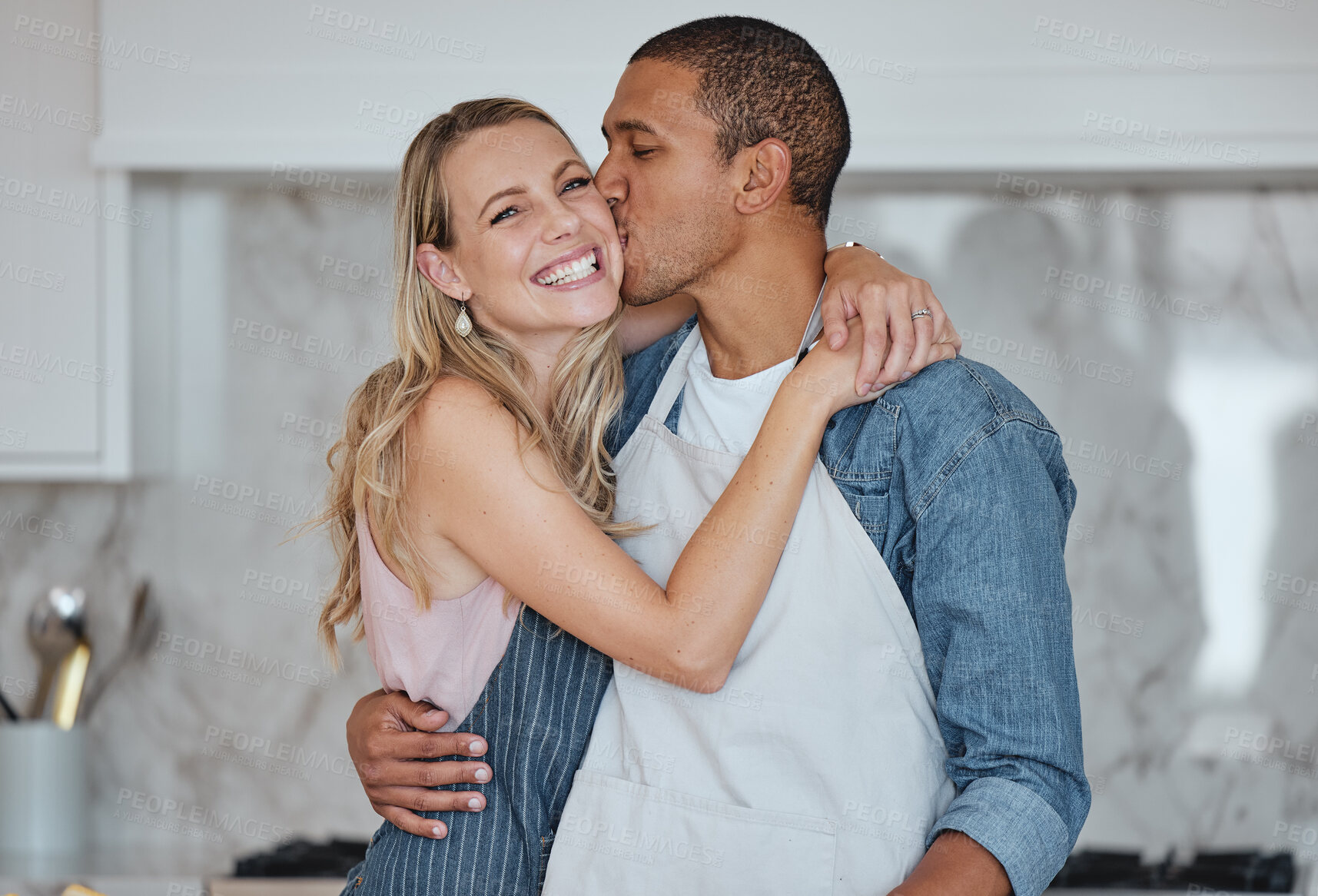 Buy stock photo Love, interracial and couple kiss in kitchen, happiness and loving together for relationship. Romance, man and woman with embrace, kissing and celebrate for anniversary, cooking and relax with hug.