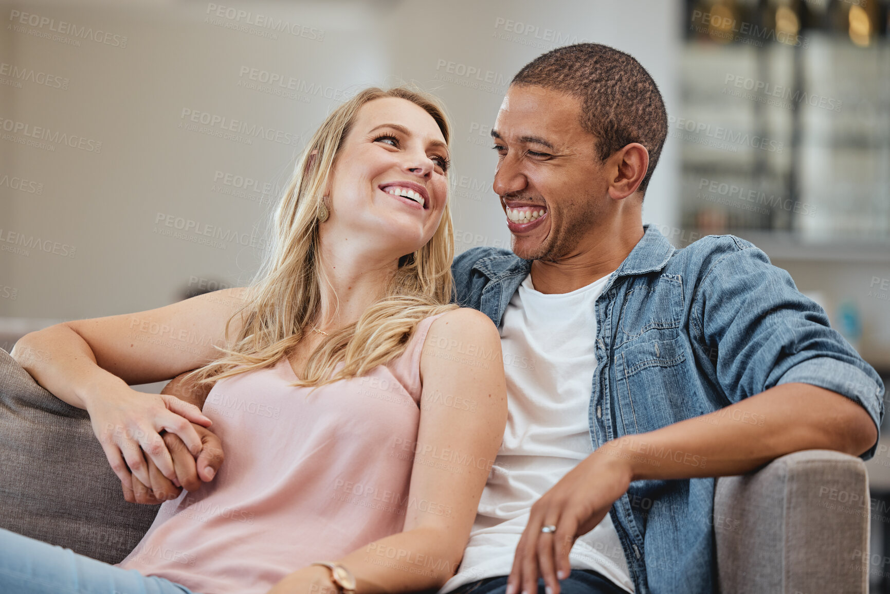 Buy stock photo Love, holding hands and smile with a interracial couple sitting on a sofa in the living room of their home together. Trust, happy and content with a man and woman bonding in their house on a weekend