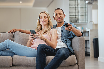 Buy stock photo Love, interracial and couple on sofa, relax or watching tv for quality time, weekend or break. Romantic, man with remote for soccer or woman with smartphone for social media, connection and streaming