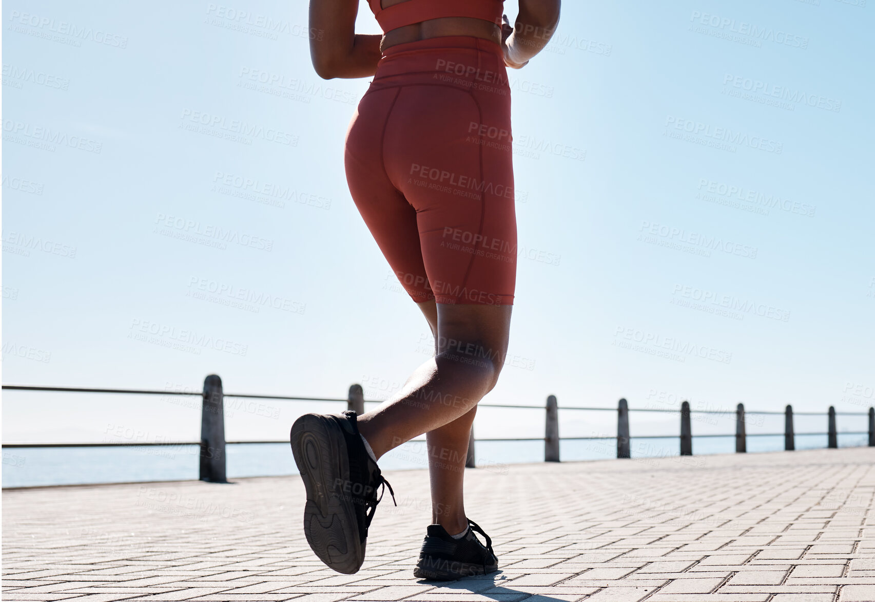 Buy stock photo Black woman, legs and running for fitness at beach sidewalk, energy and strong summer body. Runner, healthy female and sports wellness at ocean for marathon, cardio exercise and workout on blue sky