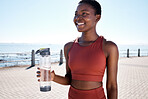 Fitness, water and black woman runner at beach for training, wellness and cardio by ocean, smile and happy. Exercise, drinking water and woman relax after running, workout and walk with hydration
