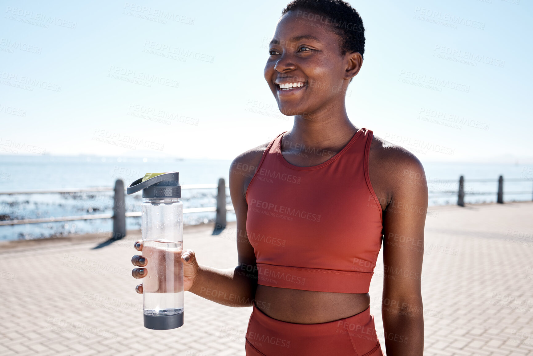 Buy stock photo Fitness, water and black woman runner at beach for training, wellness and cardio by ocean, smile and happy. Exercise, drinking water and woman relax after running, workout and walk with hydration