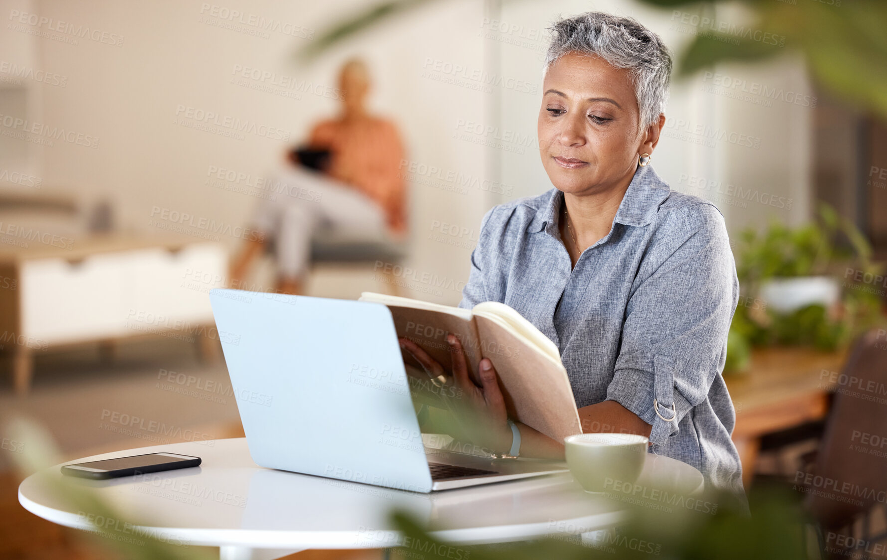 Buy stock photo Laptop, book and senior woman reading while doing research for a project in the modern office. Technology, coffee and mature female marketing professional enjoying a novel story in her workplace.
