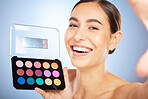 Face selfie, beauty and woman with makeup kit in studio isolated on blue background. Skincare, cosmetics product and happy female model taking pictures holding eyeshadow palette, color box and mirror