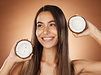 Woman, skincare and coconut in studio, happy or smile for self care, nutrition or cosmetic health. Model, skin wellness and fruit for oil, moisturizer or cosmetics background for natural radiant glow
