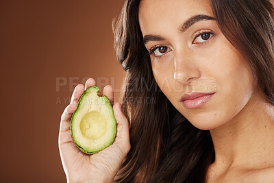 Buy stock photo Face portrait, skincare and woman with avocado in studio on a brown background. Beauty, organic cosmetics and young female model with fruit, product or food for healthy diet, nutrition and vitamin c