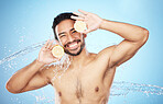 Portrait, water and lemon with a man model in studio on a blue background for natural hydration or hygiene. Face, fruit and beauty with a handsome young male wet from a water splash in the bathroom