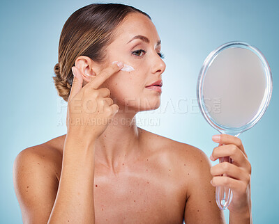 Buy stock photo Woman, face and cream with hand mirror for beauty wellness, skincare dermatology and cosmetics moisturizer in blue background studio. Model, apply sunscreen and makeup facial product for self care
