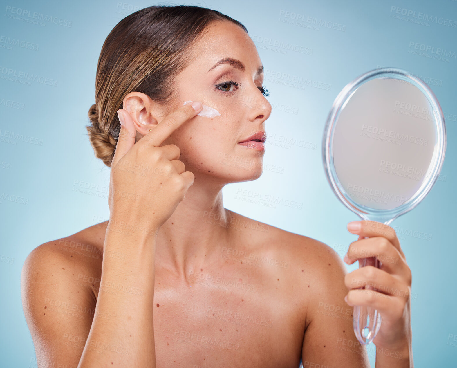 Buy stock photo Woman, face and cream with hand mirror for beauty wellness, skincare dermatology and cosmetics moisturizer in blue background studio. Model, apply sunscreen and makeup facial product for self care