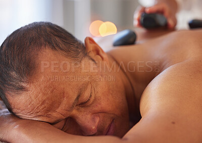 Buy stock photo Spa, man and stone massage to relax, wellness and health for body care, peace and holistic care. Male, gentleman and lying on table at luxury resort, zen and therapy for skincare and stress relief.