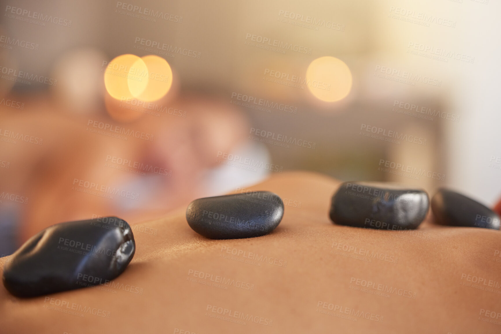 Buy stock photo Stone, man or woman at a spa for a massage, relaxing self care or luxury physical therapy healing for back pain. Hot stone massage, zoom or customer on a bed for healthy natural holistic treatment 