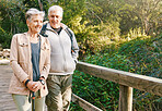 Senior hiking couple, bridge and nature on outdoor adventure, summer sunshine or bonding together. Elderly man, old woman and happiness with smile, love or walking in woods, forest or park for health