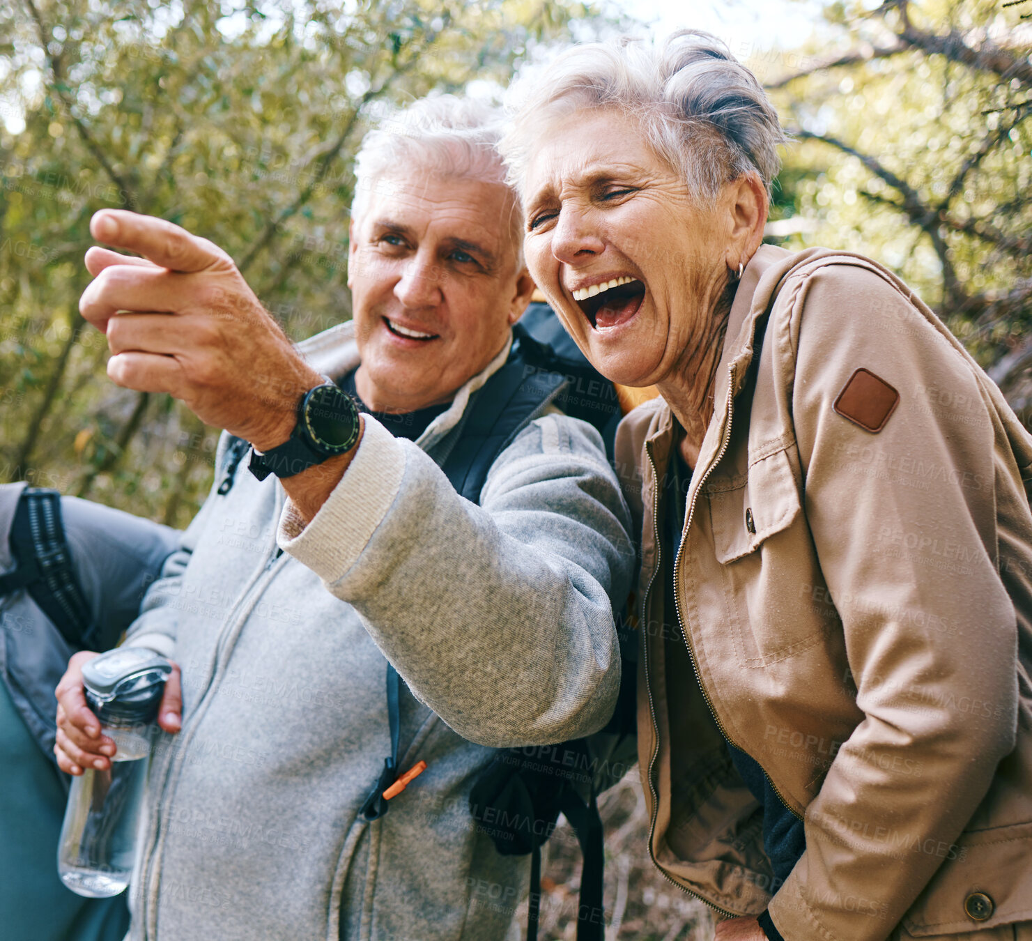 Buy stock photo Senior hiking couple, funny and outdoor adventure by trees, woods or forest for health in summer. Elderly man, pointing and woman with comic joke, laugh and bonding together for wellness in sunshine
